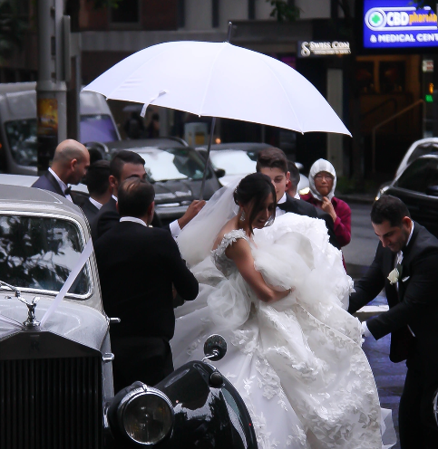 bride getting out of a car with men holding a white umbrella over her head