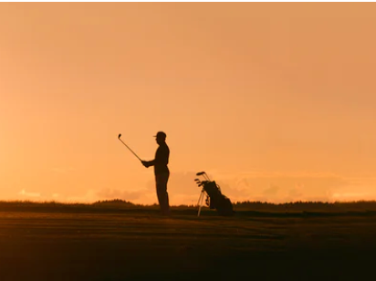 man holding golf club at sunset